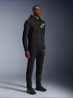 Alpinestars Chrome V2 Sport Hoodie, black motorcycle hoodie with white star logo, worn by a male model with matching black pants and riding sneakers, urban lifestyle riding gear