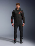 Alpinestars Chrome Air Sport Hoodie, Black and Red Fluo, Urban Motorcycle Riding Jacket with tech fleece construction, featuring a large red Astars logo on the chest and branding on the sleeve, worn by a model with black pants and riding shoes