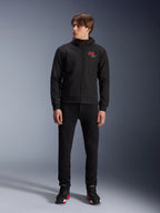 Sweat à capuche Alpinestars MM93 Radium Tech, sweat à capuche de moto urbain noir, doté d'un logo 93 rouge et d'un logo étoilé blanc sur la poitrine, porté par un mannequin avec un pantalon noir et des chaussures de moto assorties, coque technique coupe-vent élégante pour la conduite urbaine.