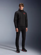 Sweat à capuche Alpinestars MM93 Radium Tech, veste de moto urbaine, noir avec des touches de rouge vif, porté par un mannequin avec un pantalon noir et des chaussures de moto, présentant le logo '93' rouge sur la poitrine et le marquage Marc Marquez sur la manche, streetwear technique décontracté pour la conduite urbaine