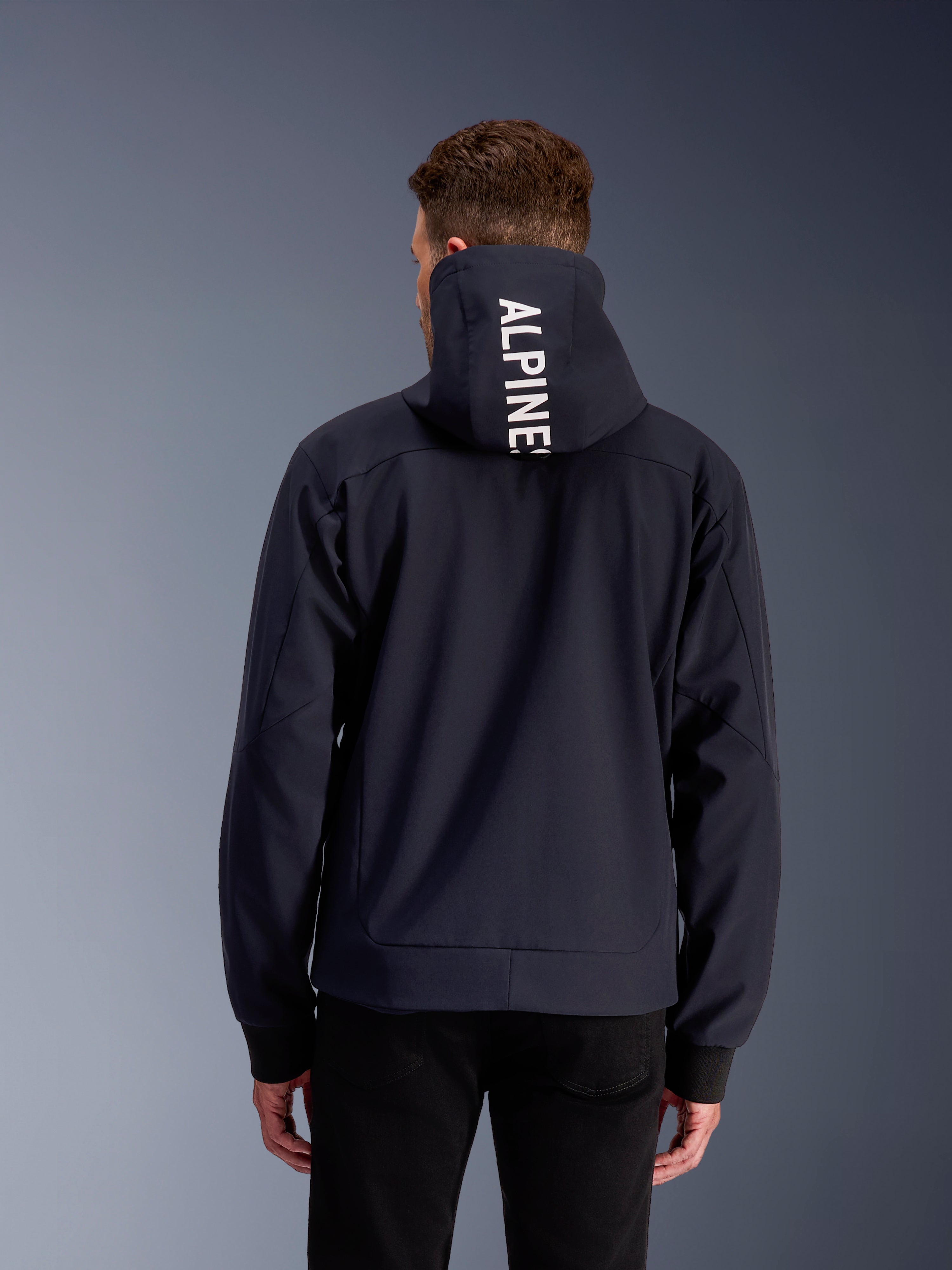 Alpinestars Sweat À Capuche Tech Radium, veste de moto urbaine pour homme, noir et blanc, vue de dos montrant le lettrage blanc sur la capuche, construction textile 3L coupe-vent et protectrice.