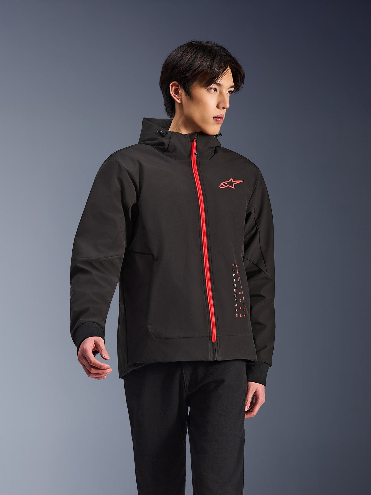 Alpinestars Radium Tech Hoodie, veste de moto urbaine, noir avec fermeture éclair rouge vif, logo Alpinestars rouge sur la poitrine et texte rouge sur le côté, coque technique coupe-vent avec capuche et poignets côtelés, style urbain moderne pour les motards