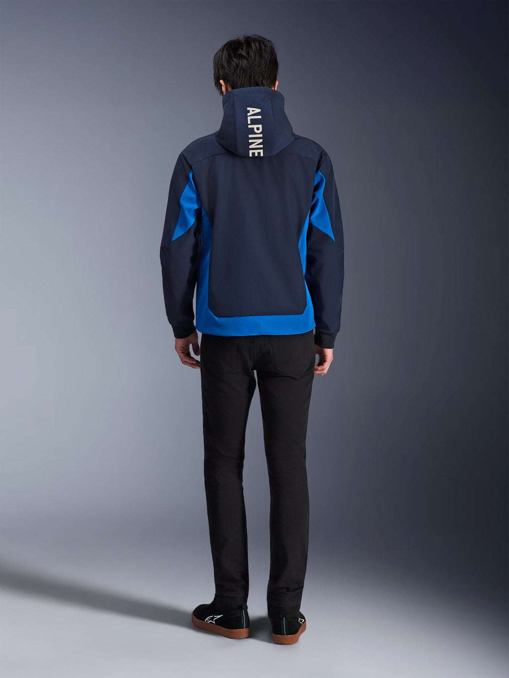Alpinestars Radium Tech Hoodie, Night Navy and Royal Blue, back view showing vertical 'ALPINE' branding on the hood, royal blue side panels and hem, casual urban motorcycle hoodie with windproof 3L shell, worn with black pants