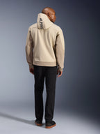 Alpinestars Radium Tech Hoodie, Mastic Aluminum, vue de dos montrant le texte vertical « ALPINE » sur la capuche, veste de moto urbaine technique avec coque 3L coupe-vent et empiècements beiges, porté avec un pantalon noir