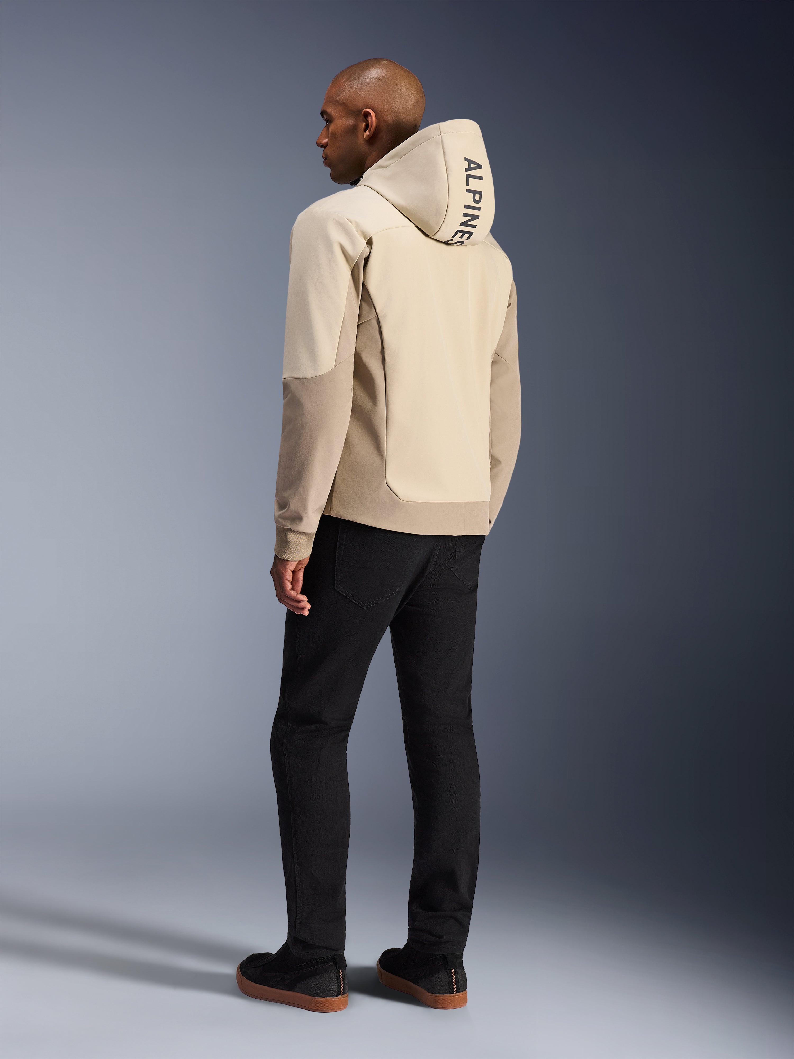 Alpinestars Radium Tech Hoodie en Mastic Aluminum, veste de moto urbaine, vue arrière sur mannequin avec capuche relevée, marquage ALPINESTARS vertical sur la capuche, associé à un pantalon noir, construction textile moderne pour la protection en conduite urbaine.