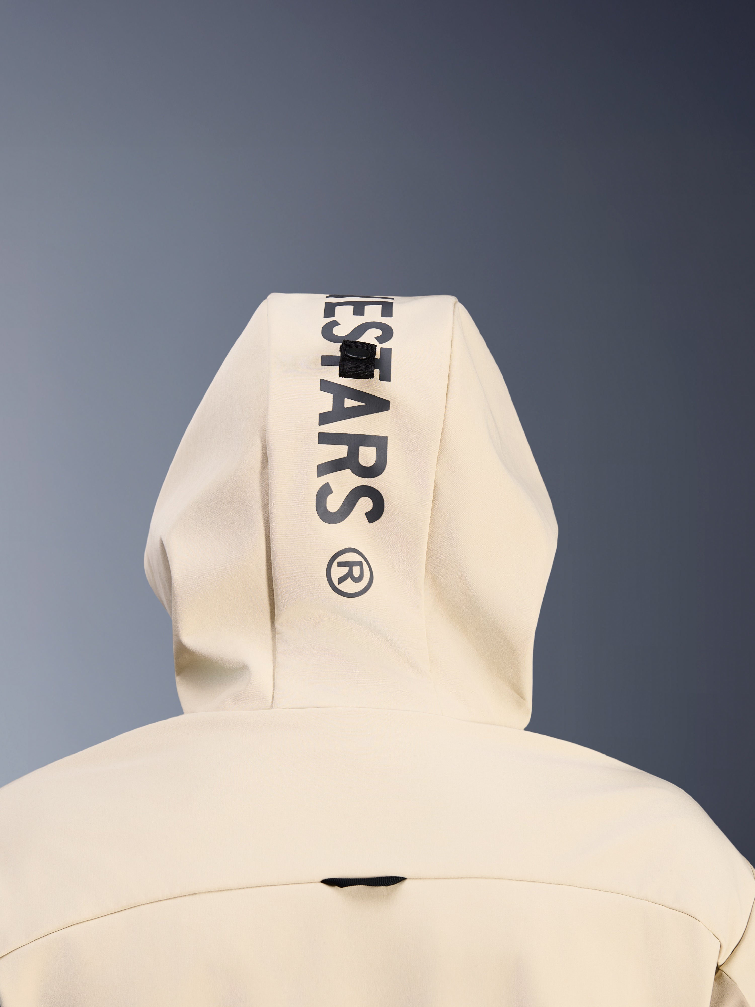 Alpinestars Radium Tech Hoodie en Mastic Aluminum, vue rapprochée de dos de la capuche montrant le marquage Alpinestars noir vertical et le système de boucle de fixation de la capuche, détail de vêtement de moto urbain