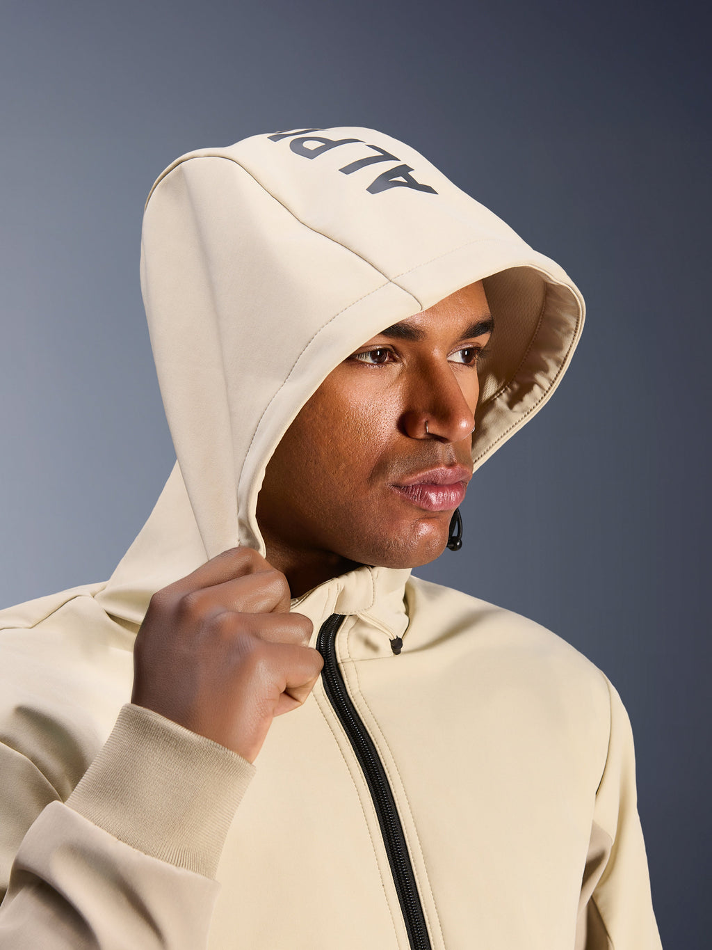 Alpinestars Radium Tech Hoodie en Mastic Aluminum, gros plan d'un homme portant la capuche relevée, avec marquage Alpinestars sur le dessus, veste de moto urbaine avec coque technique coupe-vent, esthétique streetwear moderne pour la conduite urbaine