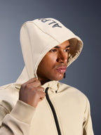 Alpinestars Radium Tech Hoodie en Mastic Aluminum, gros plan d'un homme portant la capuche relevée, avec marquage Alpinestars sur le dessus, veste de moto urbaine avec coque technique coupe-vent, esthétique streetwear moderne pour la conduite urbaine
