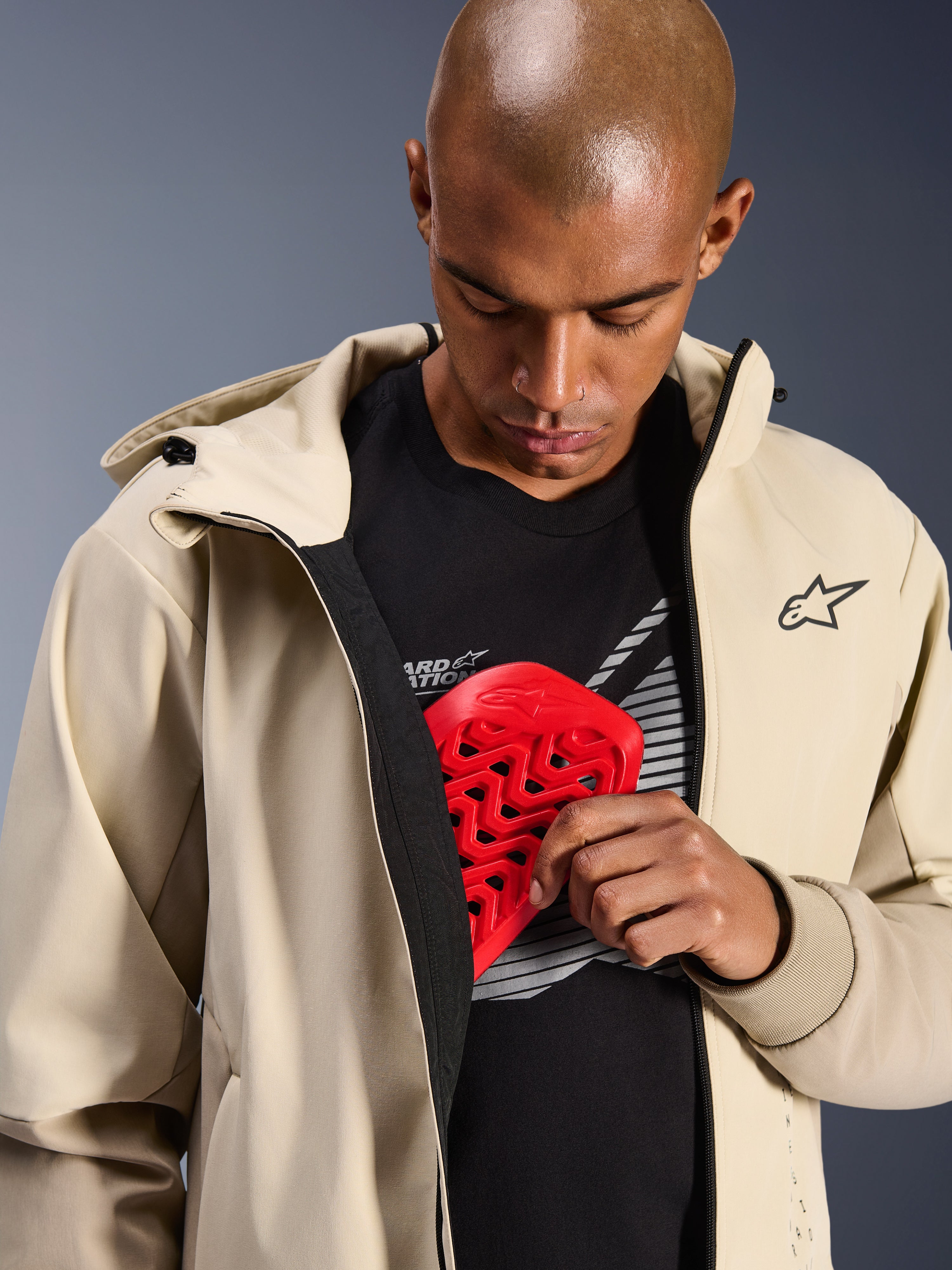 Sweat à capuche Alpinestars Radium Tech en Mastic Aluminum, veste de moto urbaine, modèle illustrant la poche de protection interne avec une protection de poitrine Nucleon rouge, coque technique coupe-vent au design décontracté avec logo Alpinestars.