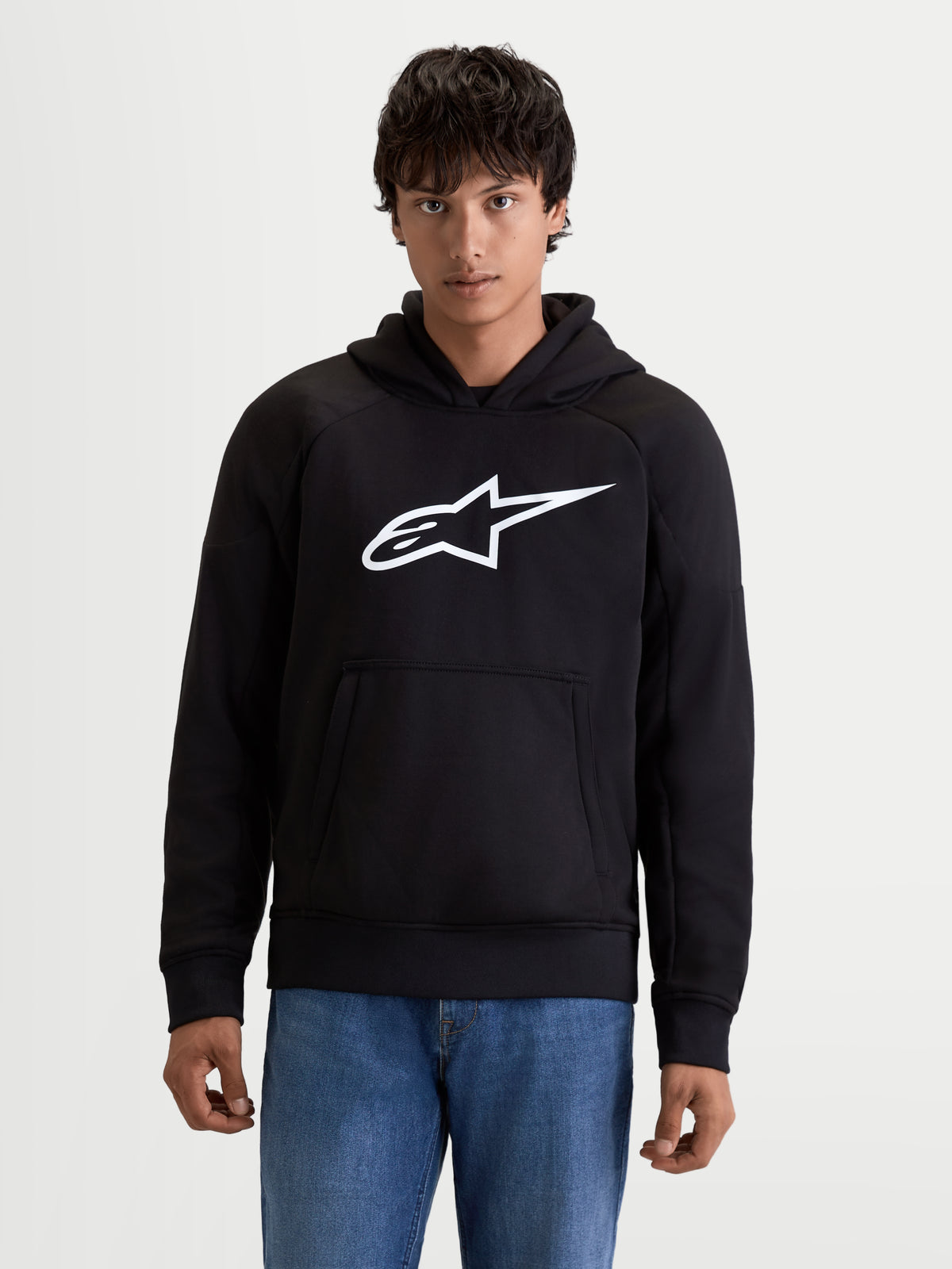 Alpinestars Sweat à Capuche Ageless, sweat de moto urbain pour homme noir avec logo blanc sur la poitrine, poche kangourou à l'avant et construction en textile décontracté, vue de face sur un modèle