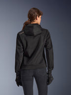 Alpinestars Stella Chrome Superairflow Hoodie, vue de dos d'une femme portant un sweat à capuche de moto technique en maille 3D noire, avec capuche technique et logo cuivré sur l'épaule, porté avec des gants et un pantalon de moto noirs.