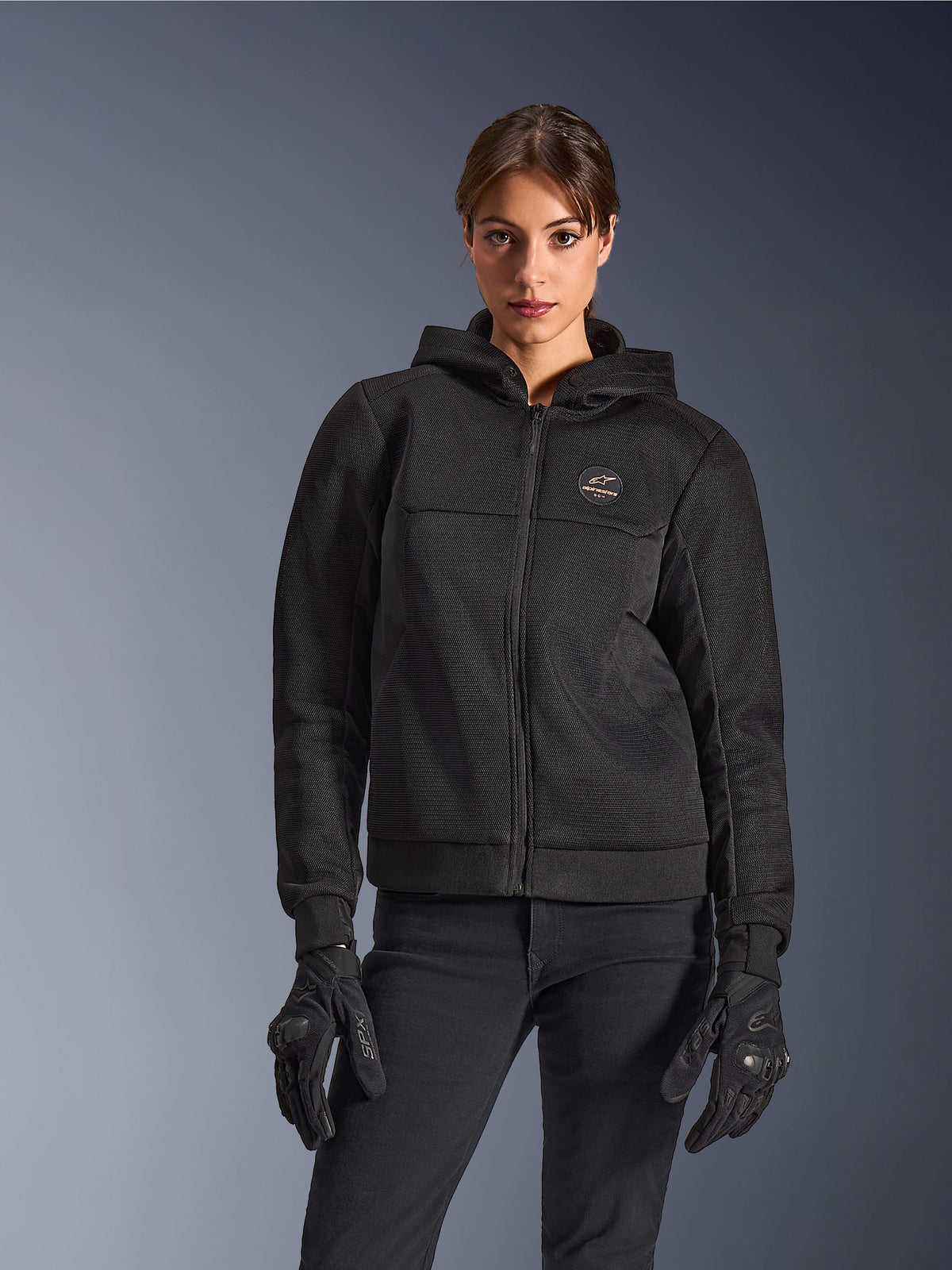 Alpinestars Stella Chrome Superairflow Hoodie, sweat à capuche de moto pour femme, noir, veste à capuche avec logo sur la poitrine et fermeture éclair centrale, portée avec des gants noirs, design moderne et épuré pour la conduite urbaine