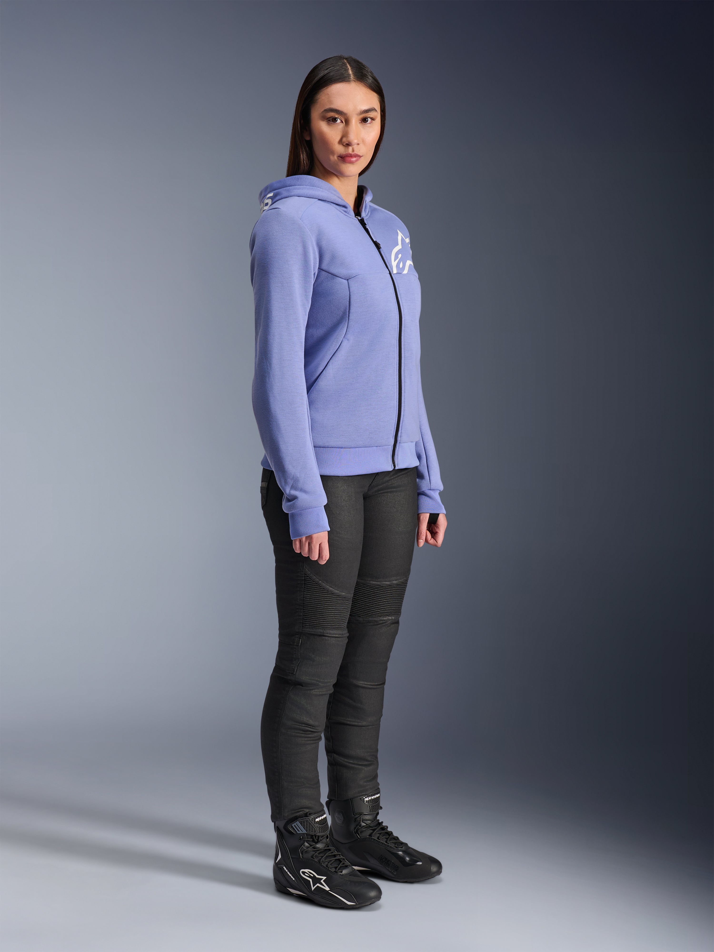 Alpinestars Stella Chrome V2 Sport Hoodie pour femme, sweat à capuche moto bleu-violet avec logo Alpinestars blanc sur la poitrine, porté par un mannequin avec un pantalon de moto noir et des bottes de moto noires, vêtement de conduite urbaine pour femme