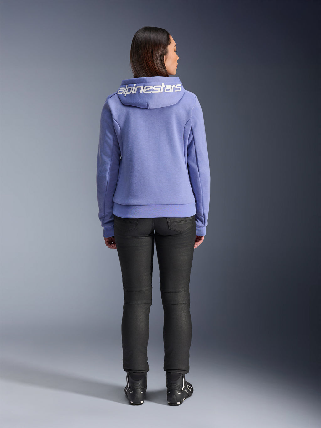 Alpinestars Stella Chrome V2 Sport Hoodie, Bleu Violet, vue de dos d'une femme portant le sweat à capuche avec logo Alpinestars blanc sur la capuche, associé à un pantalon noir et des bottes de moto, vêtement de moto urbain décontracté