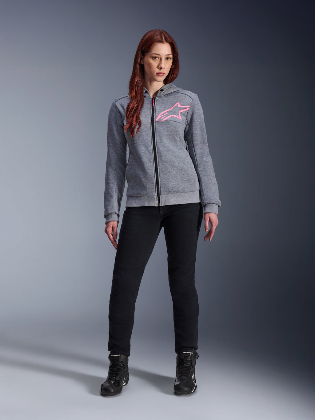 Alpinestars Stella Chrome V2 Sport Hoodie, Gray Heather Pink Fluo, worn by a woman with black pants and boots, featuring a pink Alpinestars star logo on the chest, full-zip urban motorcycle gear, lightweight tech fleece with a casual athletic fit.