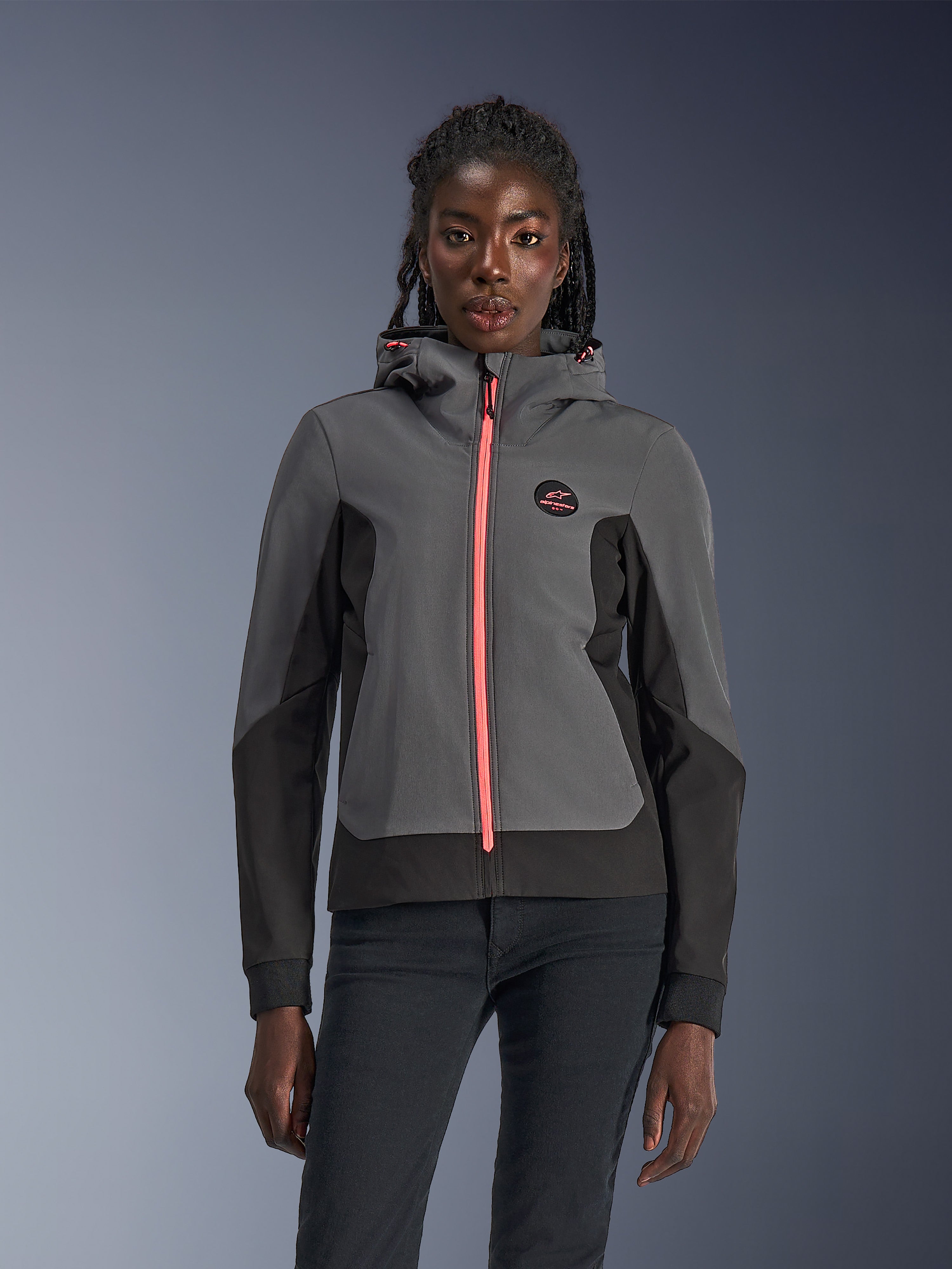 Alpinestars Stella Radium Tech Hoodie, veste à capuche de moto pour femme, gris foncé et noir avec fermeture éclair et cordons de serrage rose vif, porté par un mannequin, design urbain sportif avec logo Alpinestars sur la poitrine