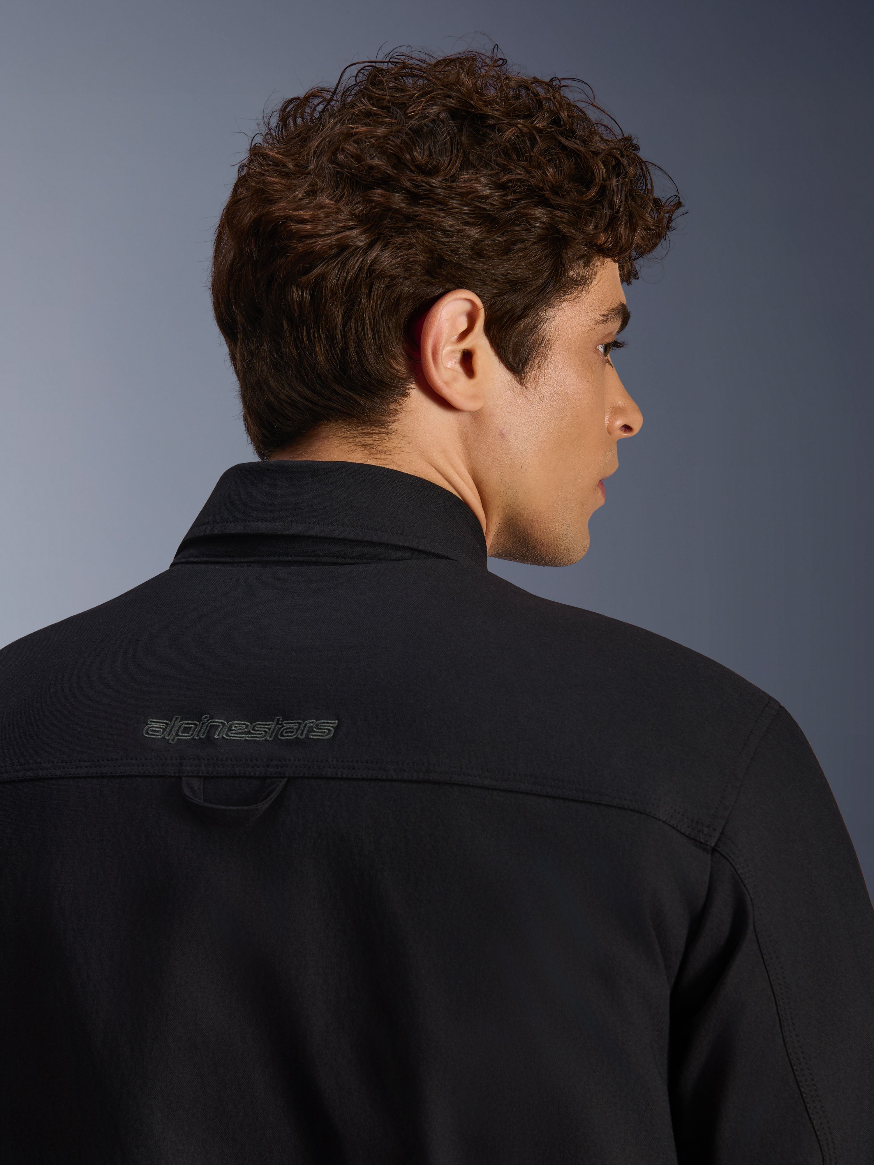 Surchemise Alpinestars Bryon Water Resistant, veste de moto urbaine, noir, gros plan de la zone de l'épaule arrière avec logo brodé et boucle de suspension, construction en toile cirée résistante à l'eau.