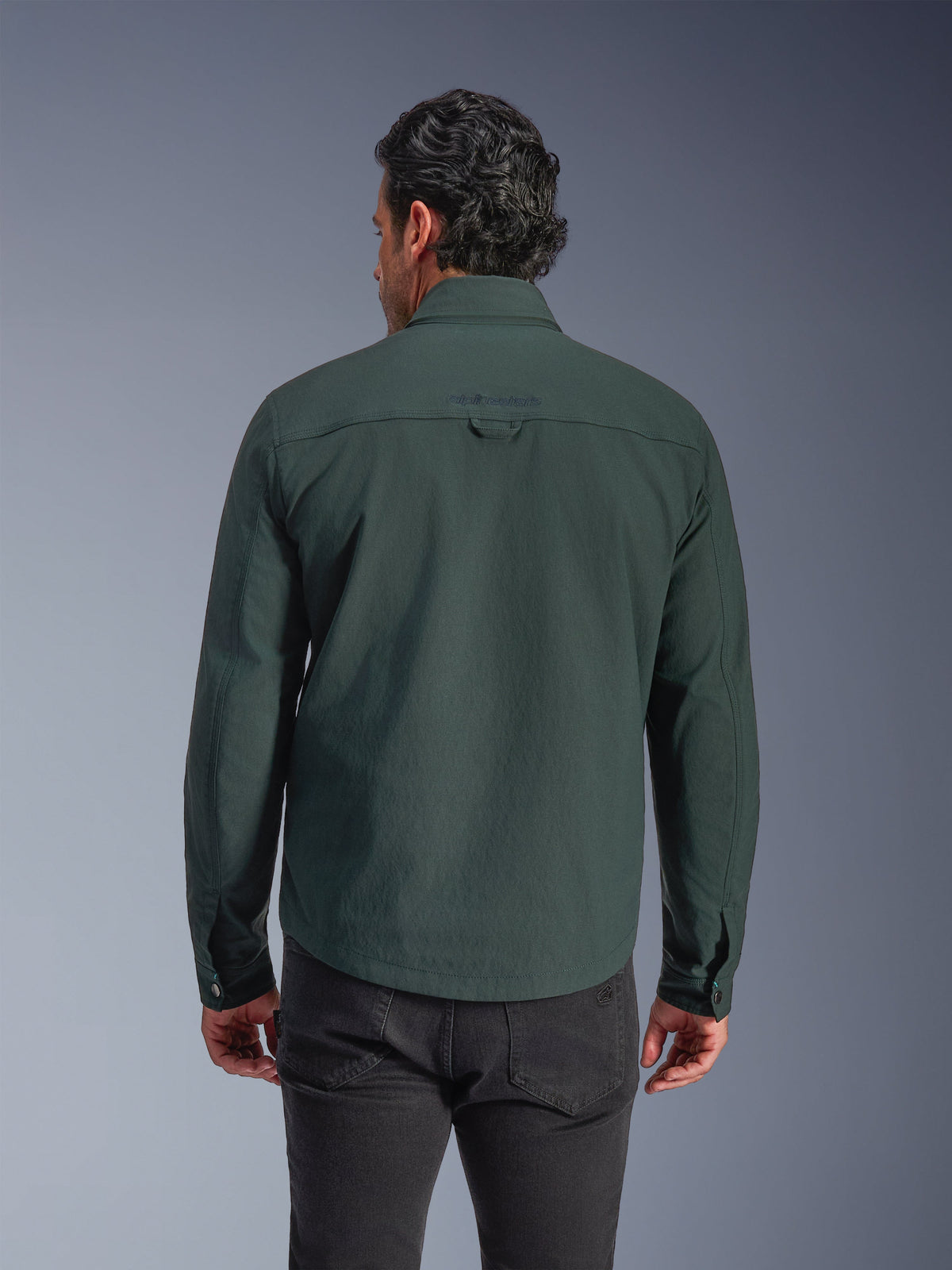 Surchemise Alpinestars Bryon Water Resistant, vert émeraude foncé, vue arrière sur modèle, logo brodé sur le haut du dos, toile cirée durable, veste de moto urbaine associée à un pantalon sombre