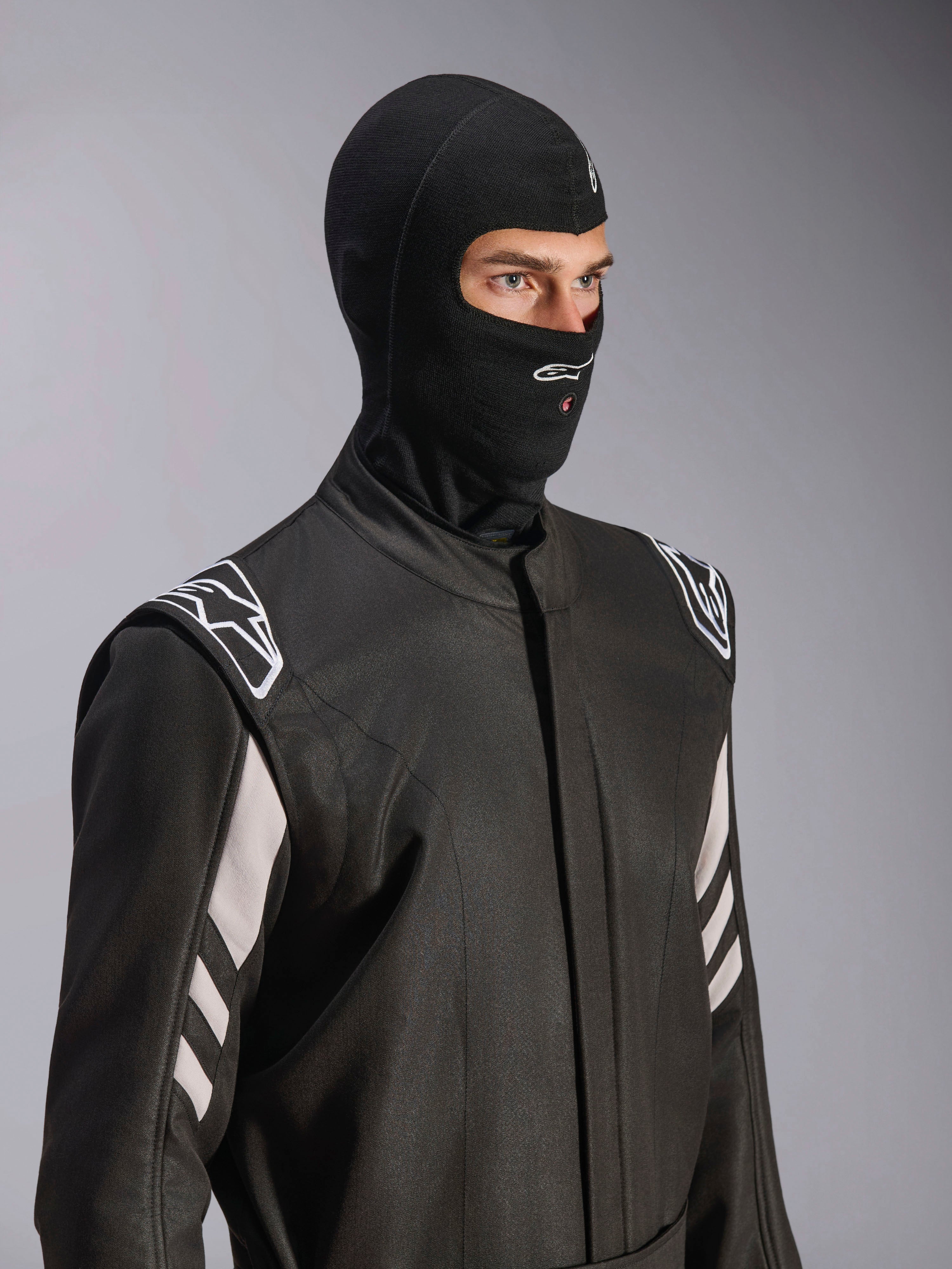 Alpinestars ZX Evo V3 Balaclava, Black, fire-resistant head sock for auto racing, worn by a model in a black racing suit with white accents, features Alpinestars logo on chin, hydration tube access port, professional motorsport protective gear