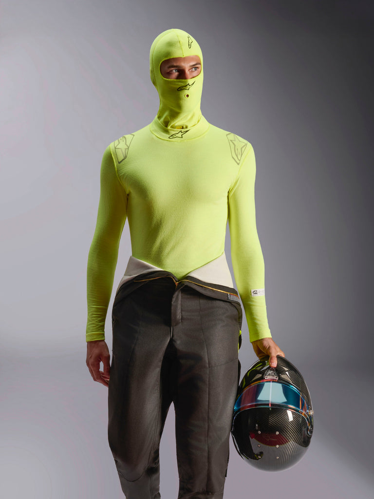 Alpinestars ZX Evo V3 Balaclava, Auto Racing Base Layer, Yellow Fluo, worn with matching long-sleeve top and racing suit pants, model holding a carbon fiber helmet with iridescent visor, professional flame-resistant motorsport gear