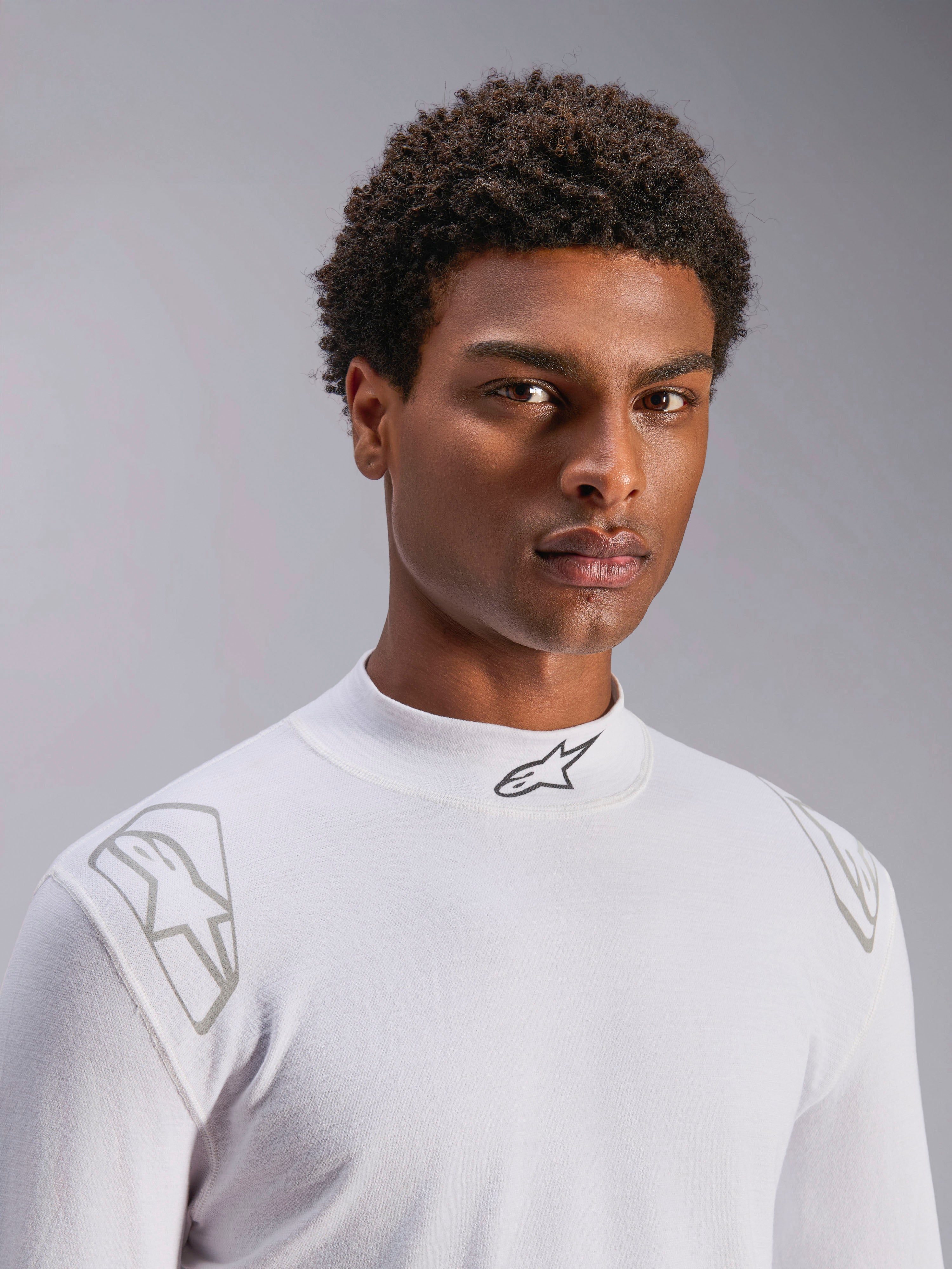 Haut à manches longues Alpinestars ZX Evo V3, sous-vêtement technique de course automobile blanc, porté par un mannequin homme, col montant avec logo Alpinestars noir, imprimés graphiques argentés sur les épaules, sous-vêtement de sport automobile léger et résistant aux flammes