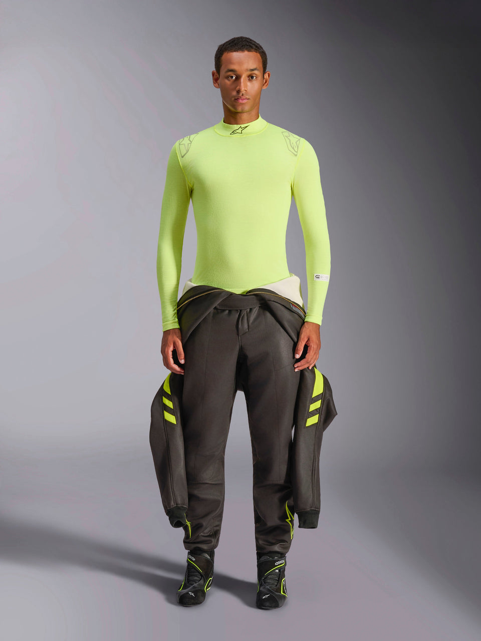 Haut à manches longues Alpinestars ZX Evo V3, jaune fluo, porté par un mannequin avec un pantalon de course sombre et des bottes, col montant et coupe athlétique, sous-couche ignifugée pour la course automobile professionnelle