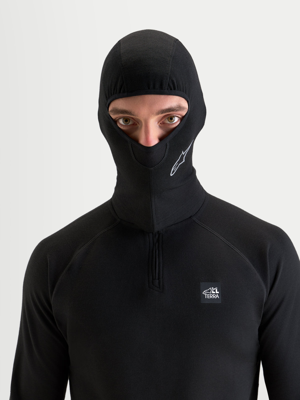 Alpinestars At 8 Merino Cagoule, cagoule de moto noire portée par un modèle avec une construction thermique en mélange de mérinos et un design à visage ouvert