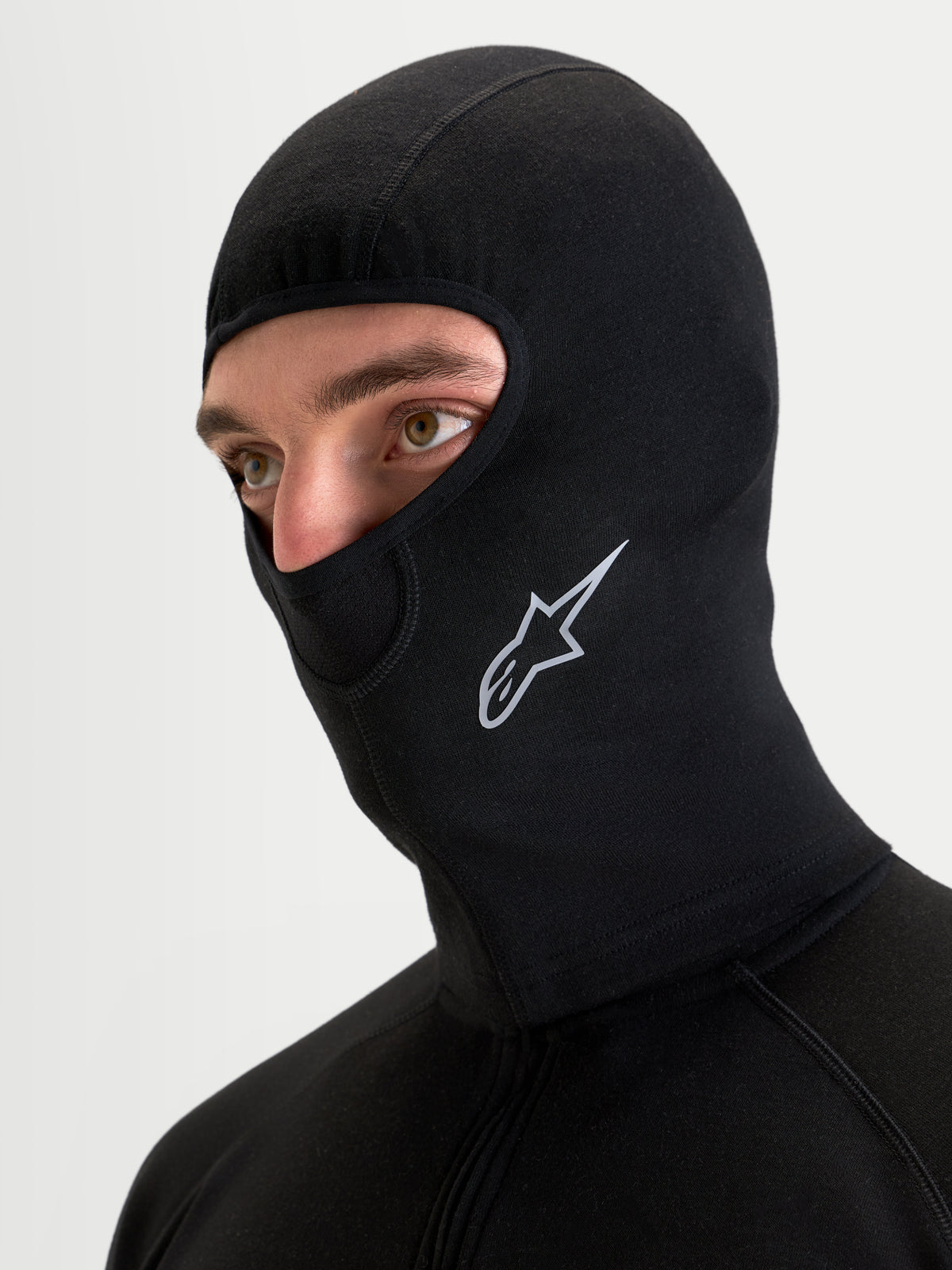 Alpinestars At 8 Merino Cagoule, cagoule thermique de moto en mélange de mérinos noire portée par un modèle, montrant les coutures plates et le logo Astar imprimé