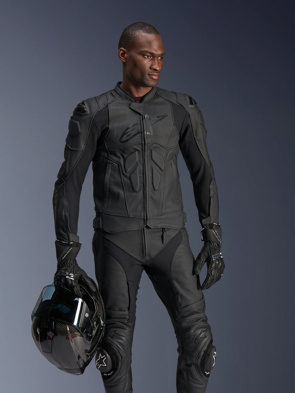 Alpinestars Dusk Airflow Leather Jacket, Black, worn by a male rider with matching leather pants and gloves, holding a black helmet, featuring perforated leather panels and integrated armor for sport motorcycle riding