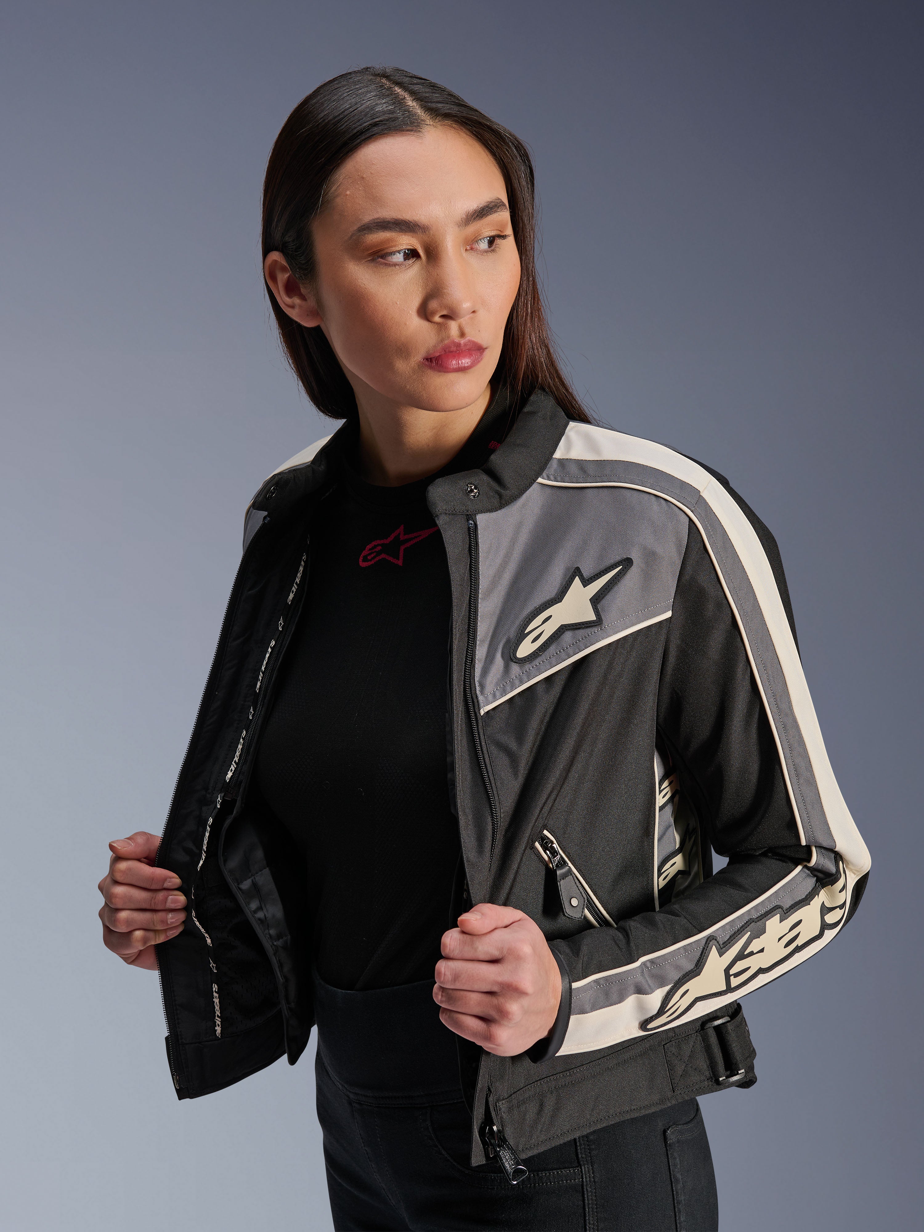 Veste Alpinestars Stella T-Dyno WR pour femme, veste de moto en textile, noir, gris foncé et écru, design d'inspiration vintage avec des bandes sportives et des logos sur la poitrine et les manches, portée par un mannequin, équipement de route urbain
