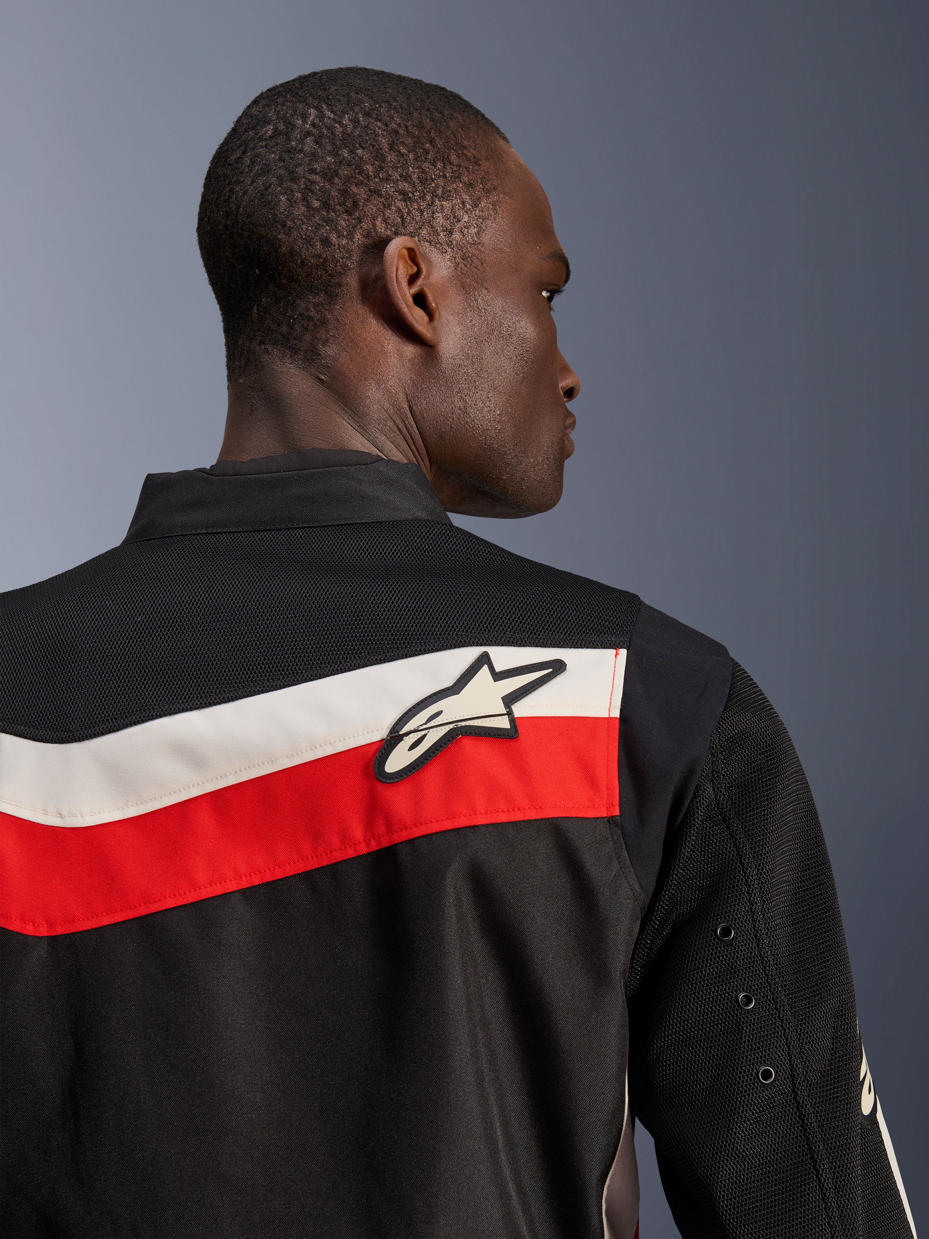 Veste Alpinestars T-Dyno Air, Noir Rouge Vif Écru, vue rapprochée du haut du dos et de l'épaule, présentant des bandes horizontales rouges et écrues avec un logo Astars blanc, panneaux en maille 3D respirante sur l'empiècement et les manches, veste de moto en textile classique moderne