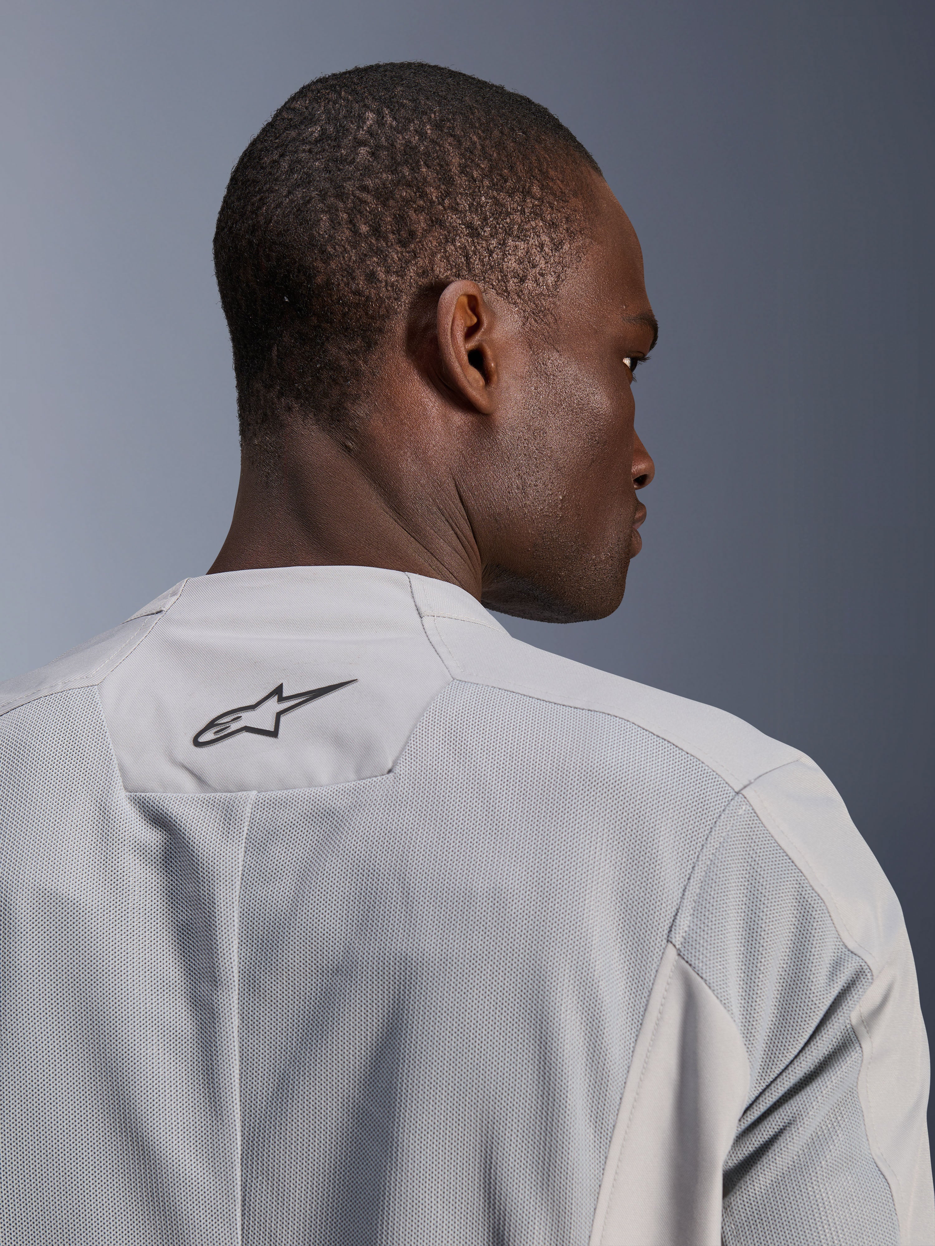 Veste Alpinestars C-1 Air, veste de moto en textile gris argenté, vue rapprochée de dos présentant des panneaux en mesh technique pour la circulation de l'air et un logo Alpinestars noir sur le haut du dos, esthétique urbaine