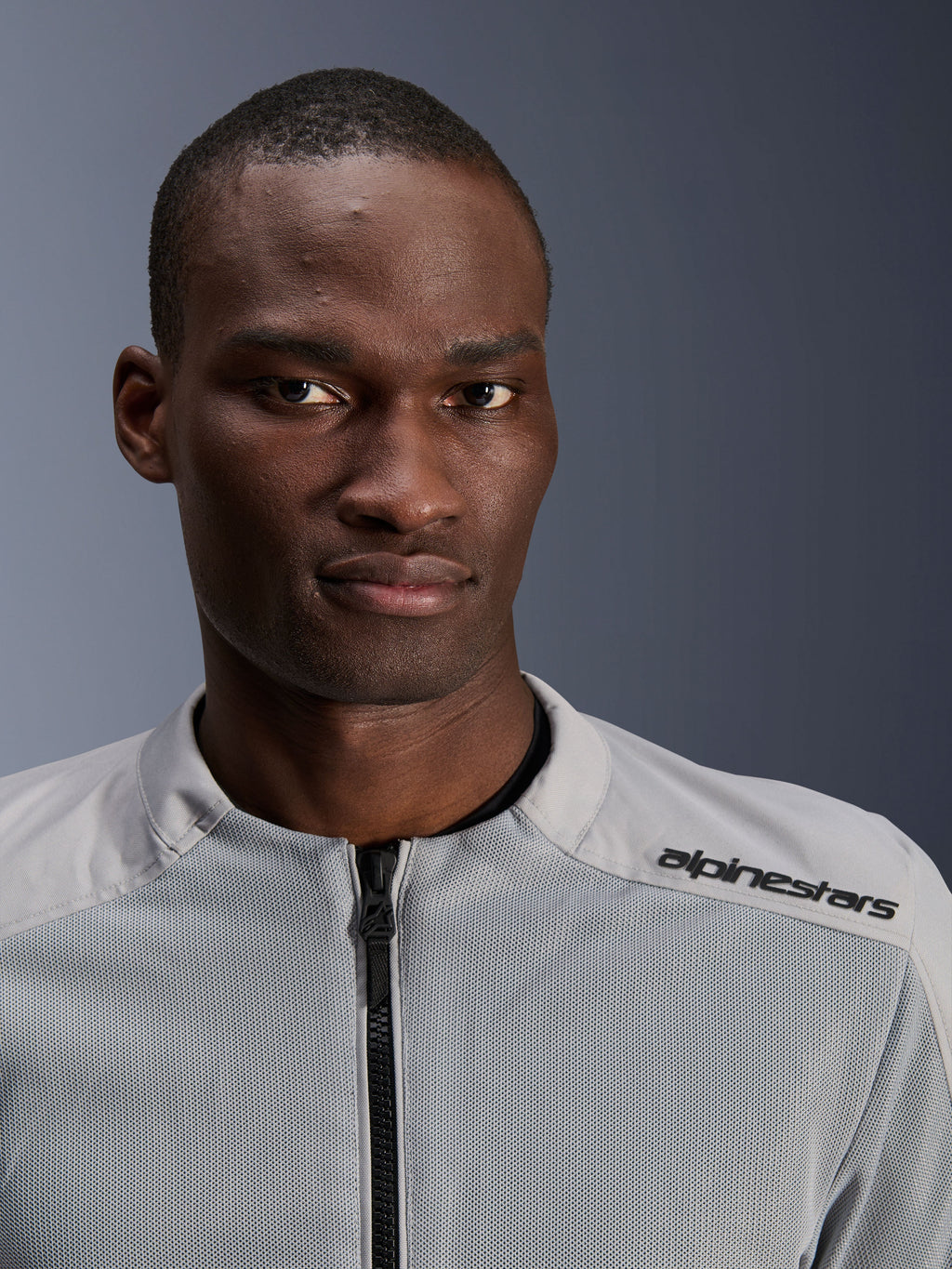Veste Alpinestars C-1 Air en argent et gris, portrait rapproché d'un motard, avec panneaux en mesh technique et marquage noir sur l'épaule, équipement de moto urbain contemporain