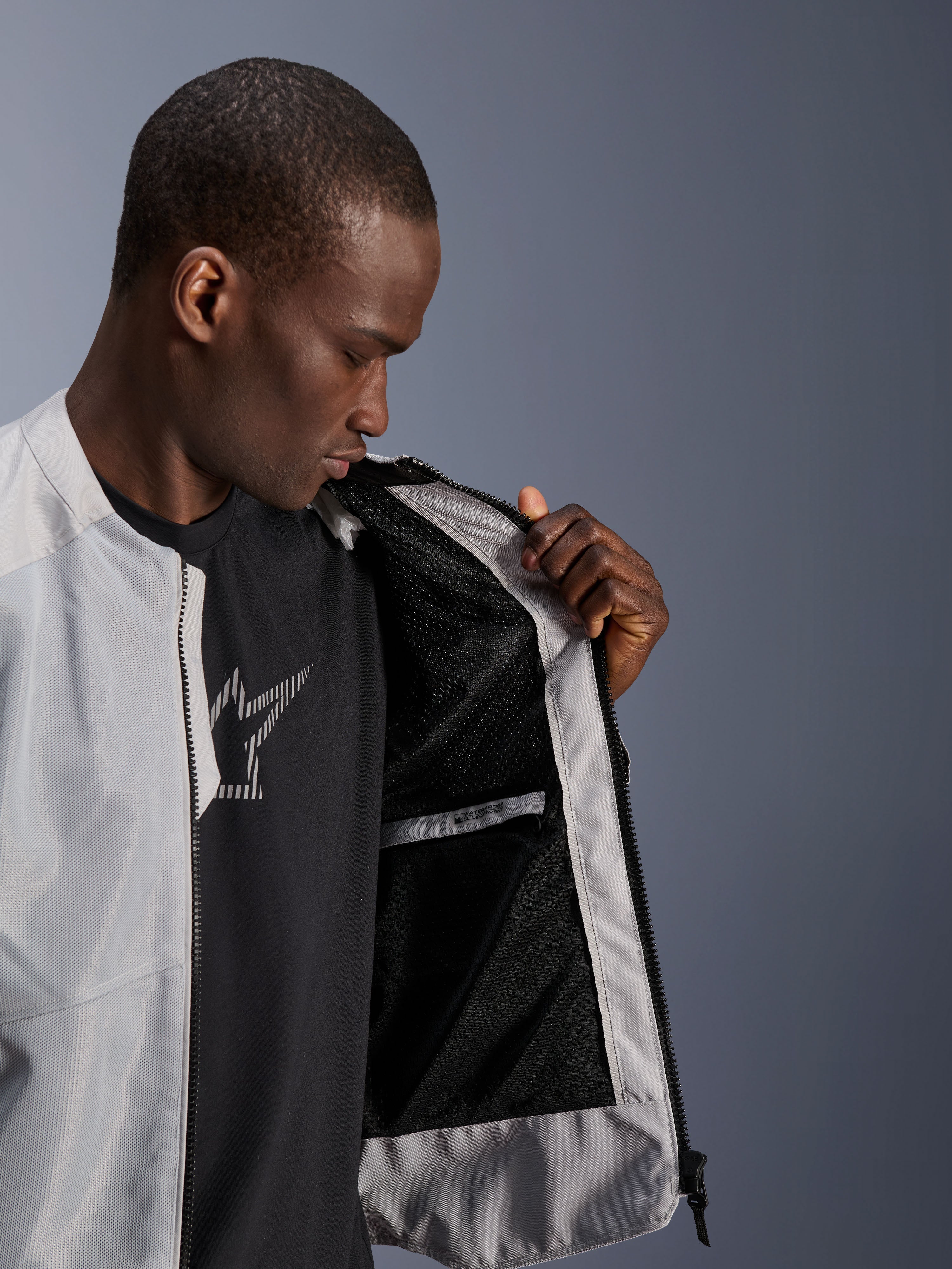 Modèle portant la veste Alpinestars C-1 Air argentée, ouvrant le devant pour révéler la doublure intérieure en mesh technique noir et une poche intérieure imperméable zippée.