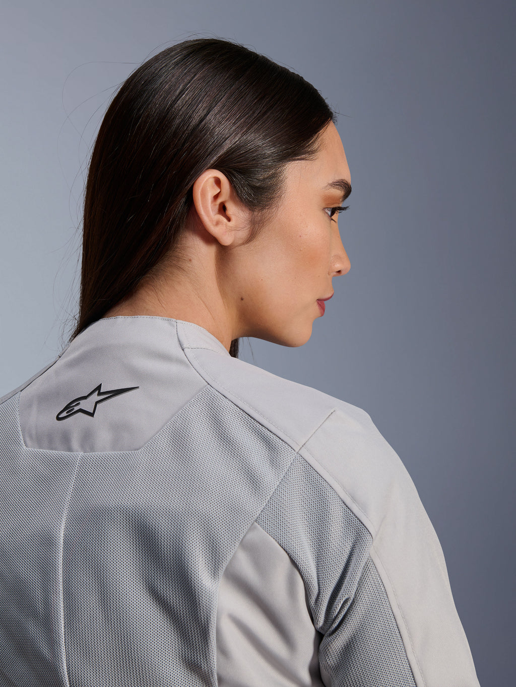 Femme portant la veste Alpinestars Stella C-1 Air en Silver, vue rapprochée de profil et de dos montrant le logo Alpinestars noir, les panneaux de ventilation en maille technique et un design de moto urbain épuré et contemporain.