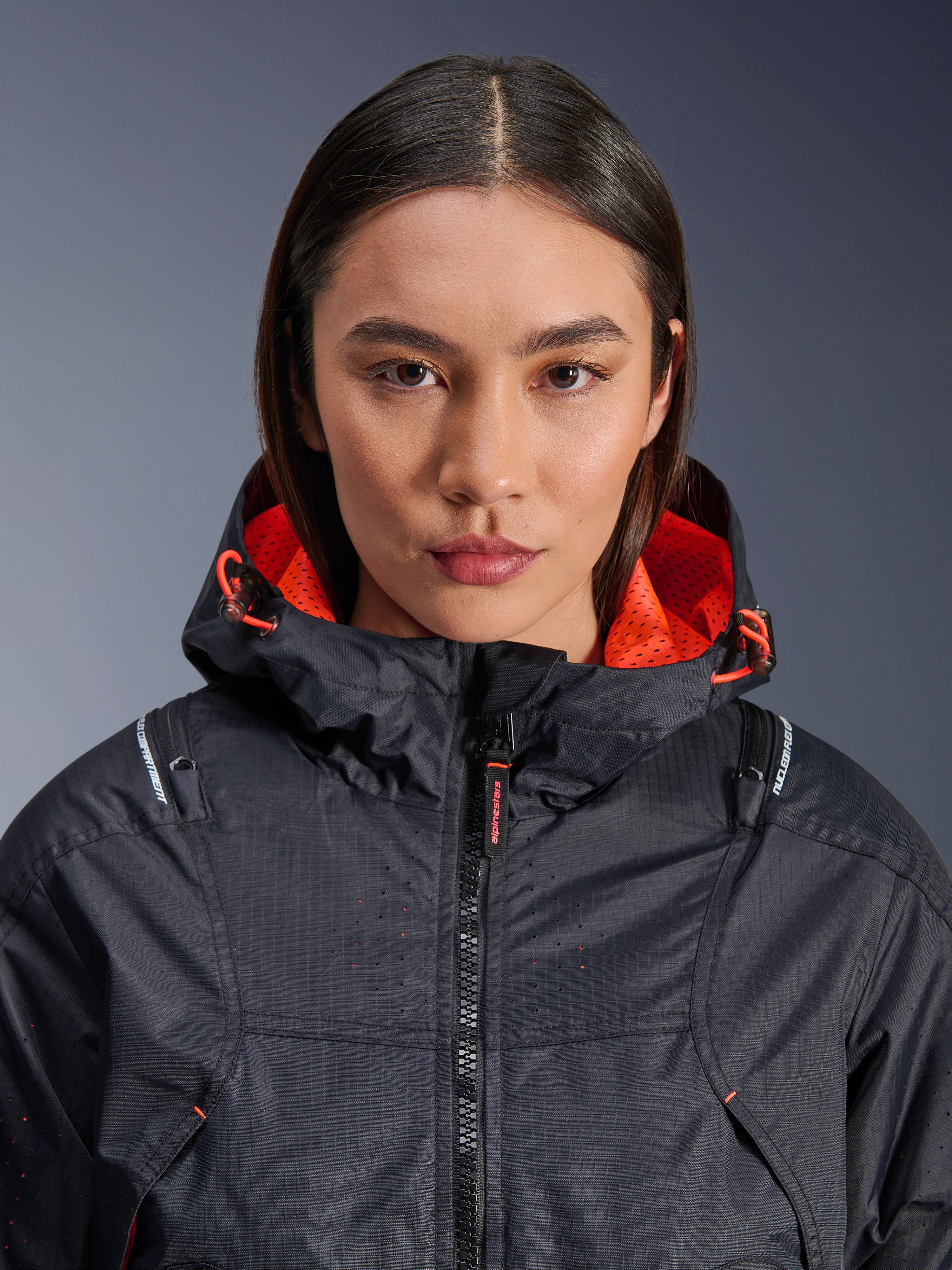 Veste Alpinestars Molly Air, veste de moto pour femme, noir et corail fluo, vue de face en gros plan sur un mannequin, textile ripstop avec ventilation perforée au laser, doublure de capuche en maille orange vif et cordons de serrage, avec marquage des protections Nucleon Flex Plus