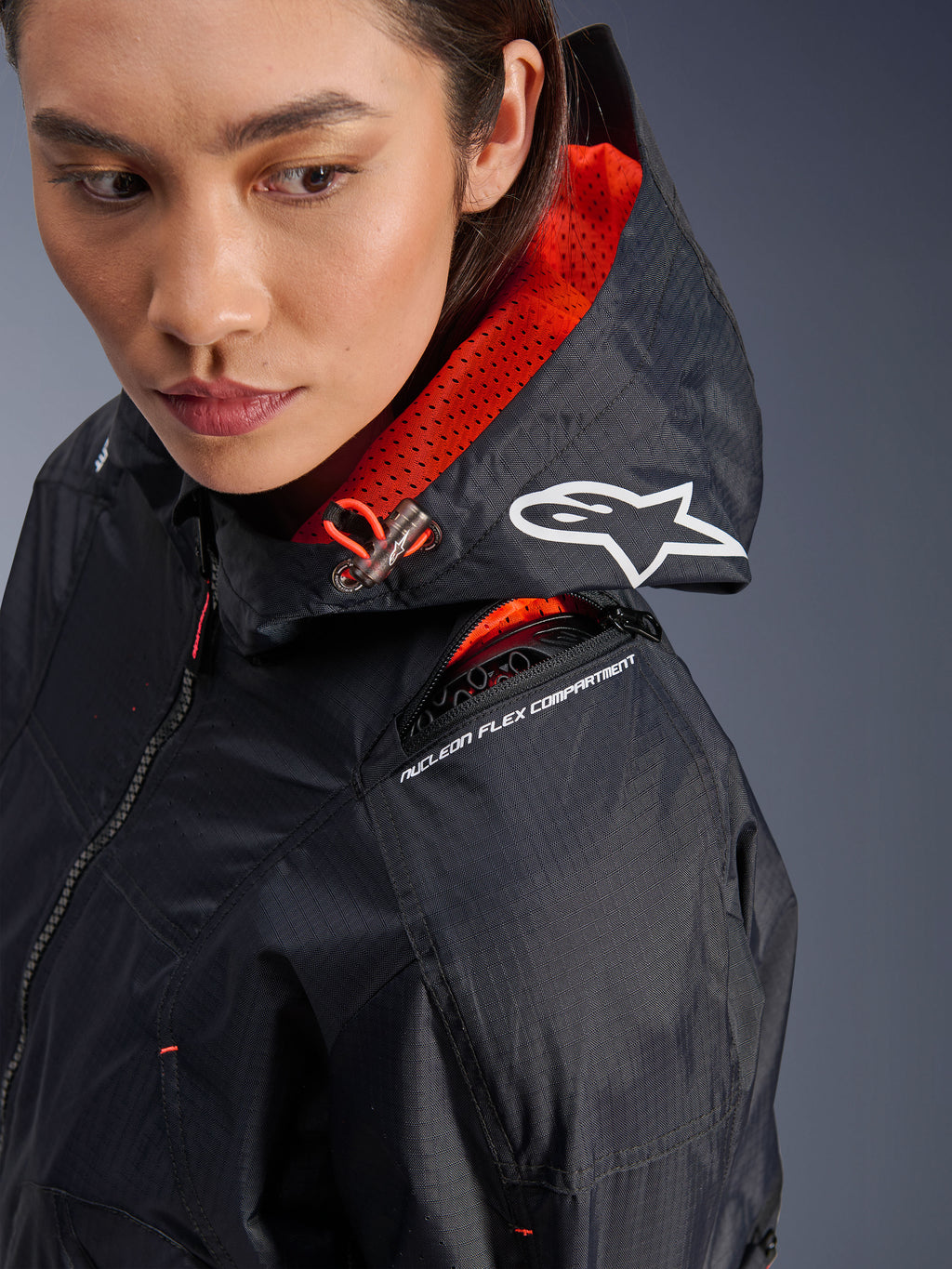 Veste Alpinestars Molly Air, veste de moto pour femme, noir et corail fluo, gros plan sur l'épaule mettant en évidence le compartiment de protection Nucleon Flex et le logo Astars blanc sur la capuche, équipement de conduite urbaine en tissu ripstop