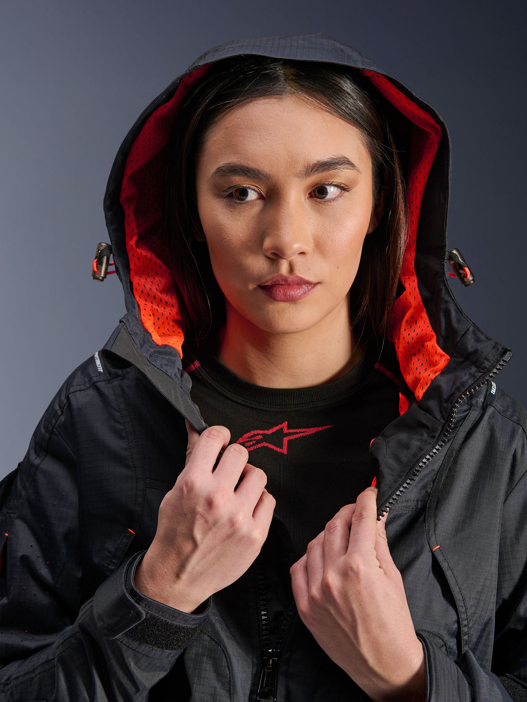 Veste Alpinestars Molly Air, veste de moto pour femme, noir et corail fluo, mannequin portant la capuche relevée montrant la doublure en maille corail vif, tissu textile ripstop, équipement de conduite urbain contemporain