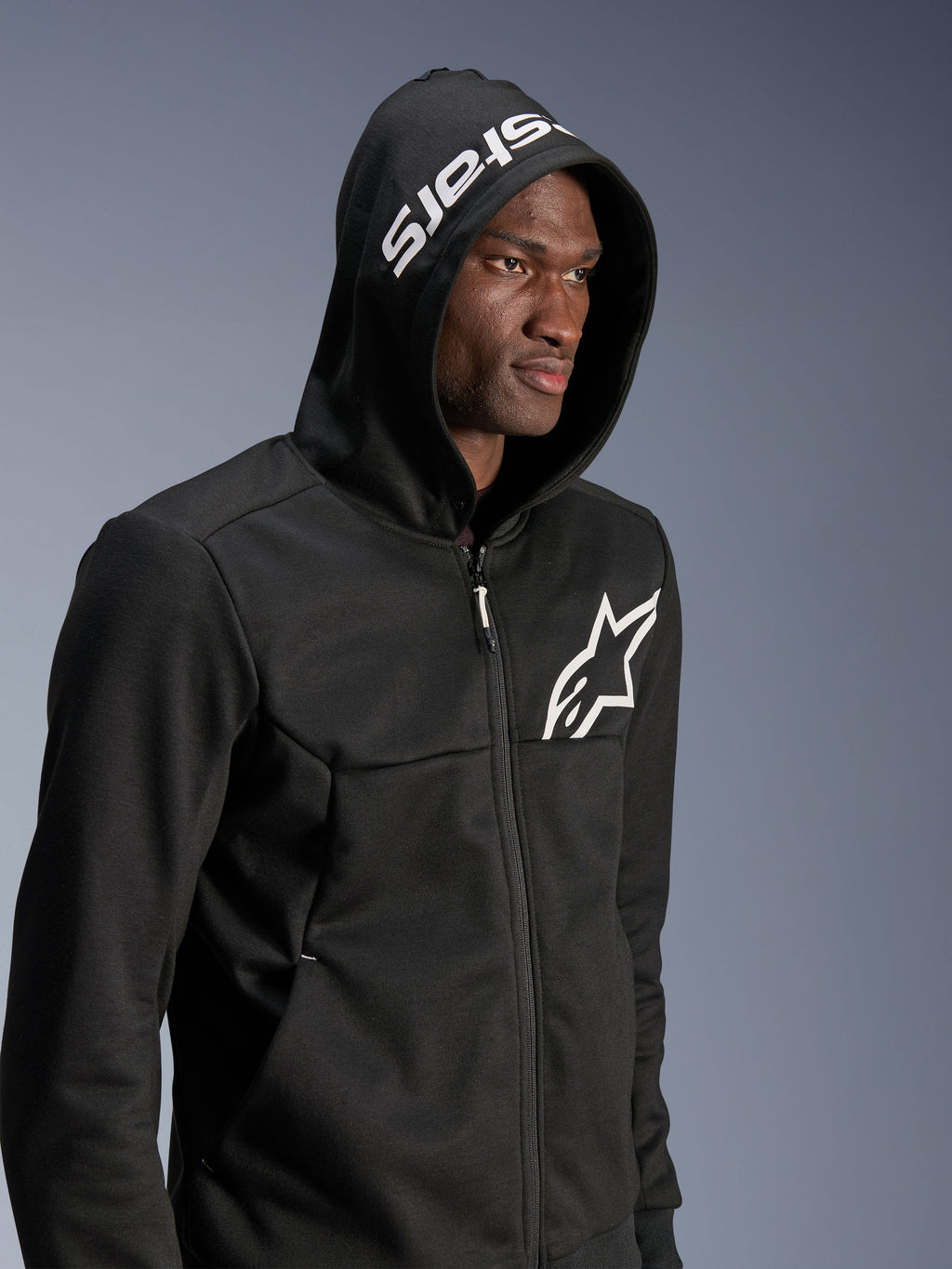 Alpinestars Chrome V2 Sport Hoodie, Black, urban riding hoodie worn by model with hood up, white star logo on chest and white stars branding on the hood, tech fleece construction, casual motorcycle streetwear