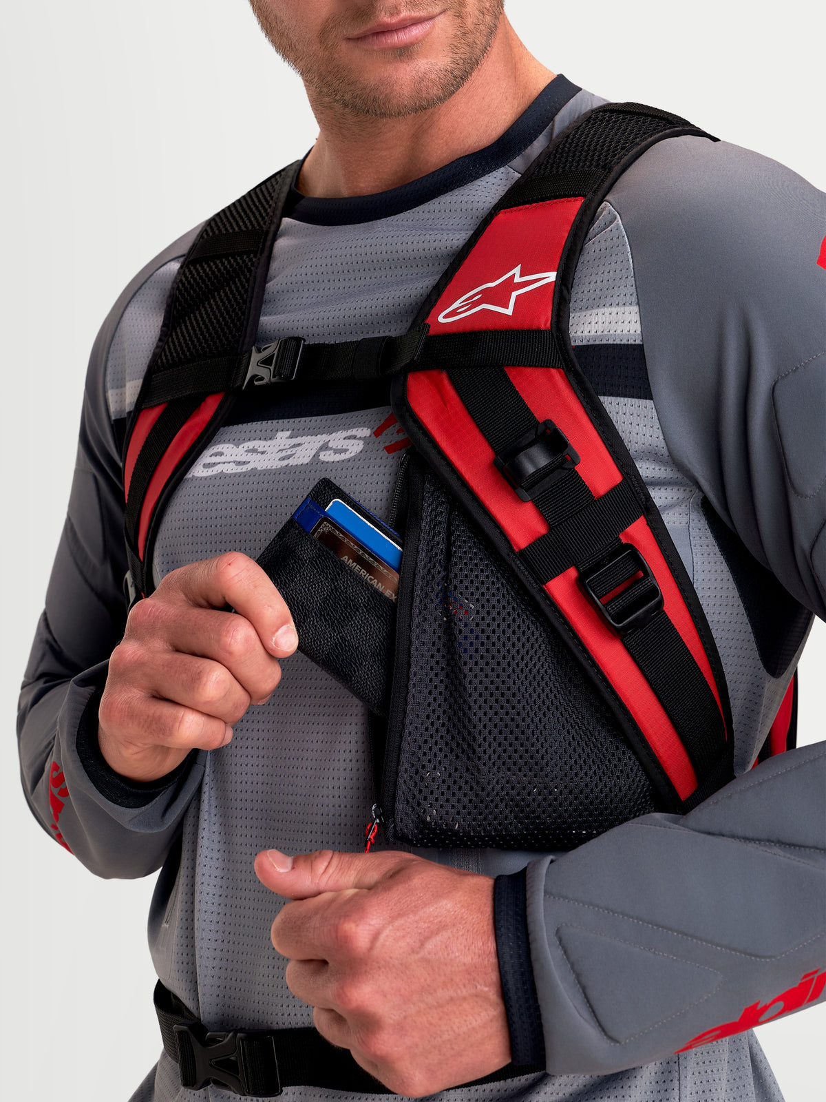 Sac à dos Alpinestars AT-9, sac à dos motocross noir et rouge vif, vue rapprochée montrant le système de harnais d'épaules rembourré et la poche zippée en résille portée par un modèle