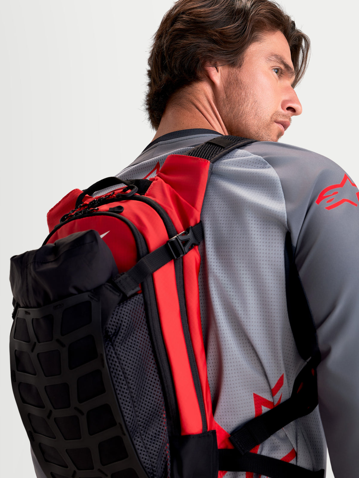 Alpinestars Sac À Dos AT-9, sac à dos de motocross noir et rouge vif, vue de dos montrant un modèle portant le sac léger doté de bretelles rembourrées