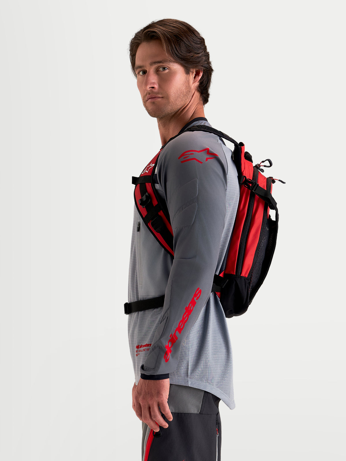 Sac à dos Alpinestars AT-9, sac à dos de moto tout-terrain noir et rouge vif, vue de profil latéral porté par un modèle masculin avec équipement MX assorti, doté d'une construction en textile léger et d'un système de harnais ergonomique