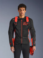 Homme portant le sac à dos Alpinestars MM93 AMP3, rouge fluo et noir, doté de bretelles réglables et d'une sangle de poitrine à boucle, assorti à une veste de moto et des gants MM93, équipement technique de la collection Marc Marquez