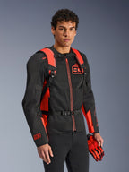 Sac à dos Alpinestars MM93 AMP3, rouge fluo et noir, porté par un modèle avec une veste de moto et des gants MM93 assortis noirs et rouges, vue de face mettant en avant les bretelles réglables et la boucle de poitrine, équipement technique inspiré de la course
