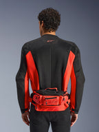 Sac banane Alpinestars MM93, rouge et noir, porté sur un blouson de moto noir et rouge, avec logo Marc Marquez 93, ceinture réglable et compartiments zippés, accessoire fonctionnel d'inspiration racing