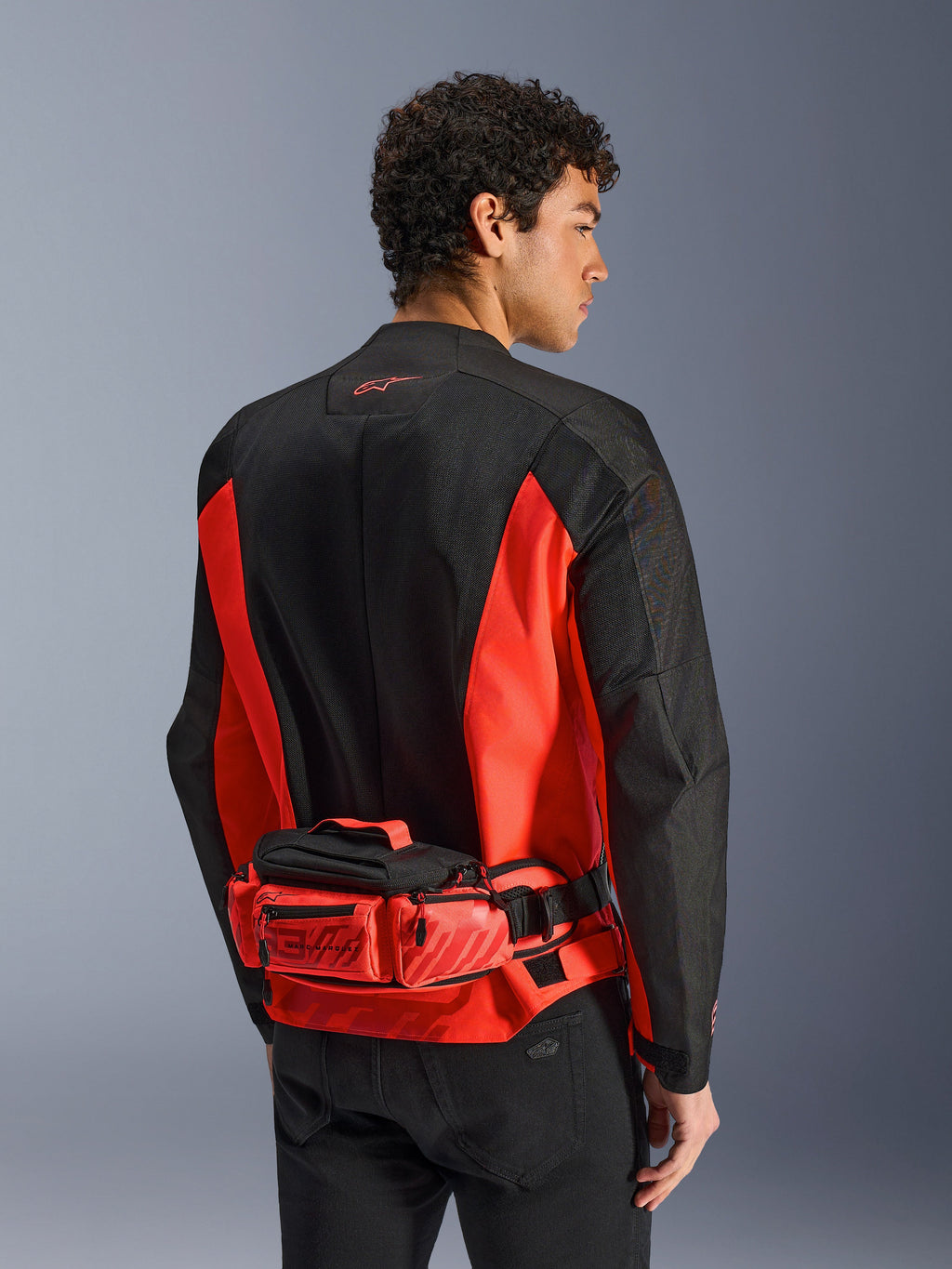 Alpinestars MM93 Waist Bag, sac banane de moto, rouge vif et noir, porté sur une veste de moto assortie noire et rouge, doté de compartiments zippés et du marquage Marc Marquez MM93, construction en textile durable pour la moto