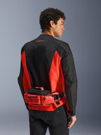 Alpinestars MM93 Waist Bag, sac banane de moto, rouge vif et noir, porté sur une veste de moto assortie noire et rouge, doté de compartiments zippés et du marquage Marc Marquez MM93, construction en textile durable pour la moto