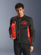 Homme portant le sac banane Alpinestars MM93, rouge fluo et noir, porté en bandoulière sur une veste de moto assortie noire et rouge, avec le logo Marc Marquez 93, design sportif de course