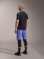 Male model from behind wearing Alpinestars A-Aria Lite Shorts in Baja Blue, paired with a black short-sleeve jersey and black knee protectors, professional MTB cycling apparel for trail riding.