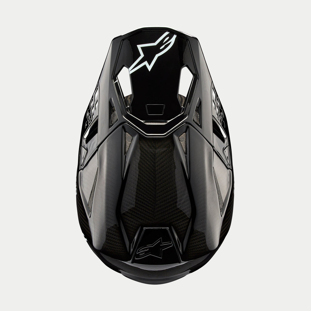 Alpinestars Supertech M10 Solid Helmet, Motocross Helmet, Black Glossy Carbon, Top-down view showing visible carbon fiber weave, white Astars logo on the visor, sleek aerodynamic profile with integrated ventilation ports